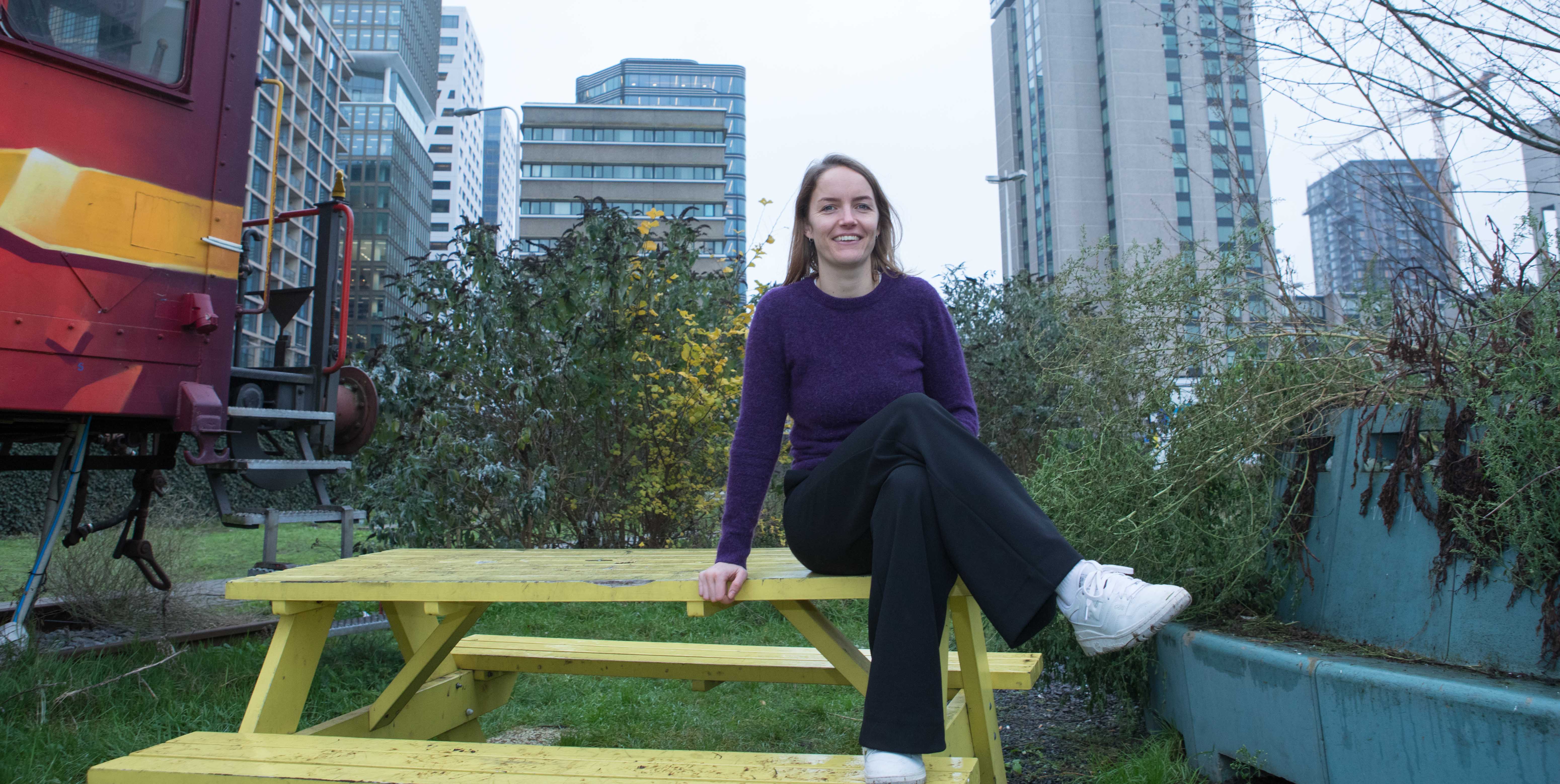 Marthe, lid van het Stadsteam, zit op een geel bankje voor haar portretfoto.