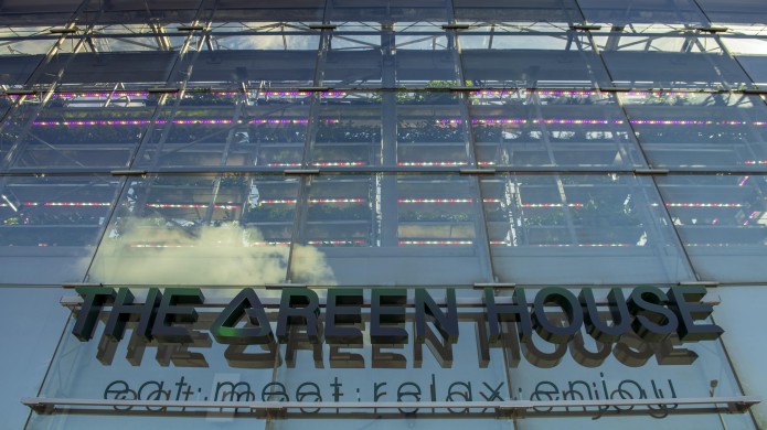 Logo van The Green House op het reflecterende gebouw. Zwarte strakke letters. Eronder staat: eat. meet. relax. enjoy.